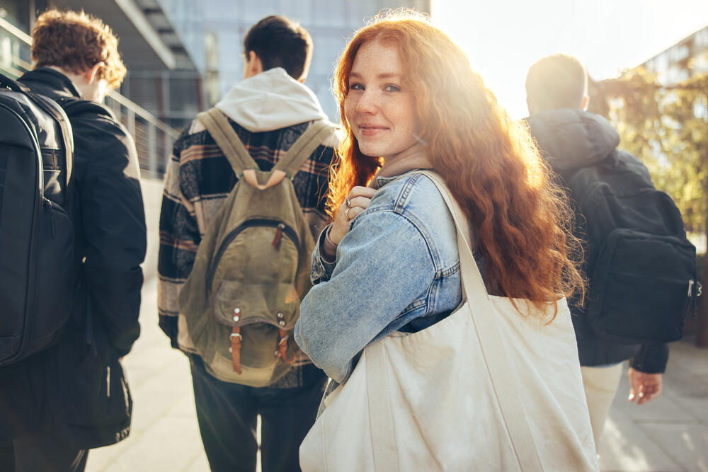 Smiling girl holding backpack and looking over her shoulder