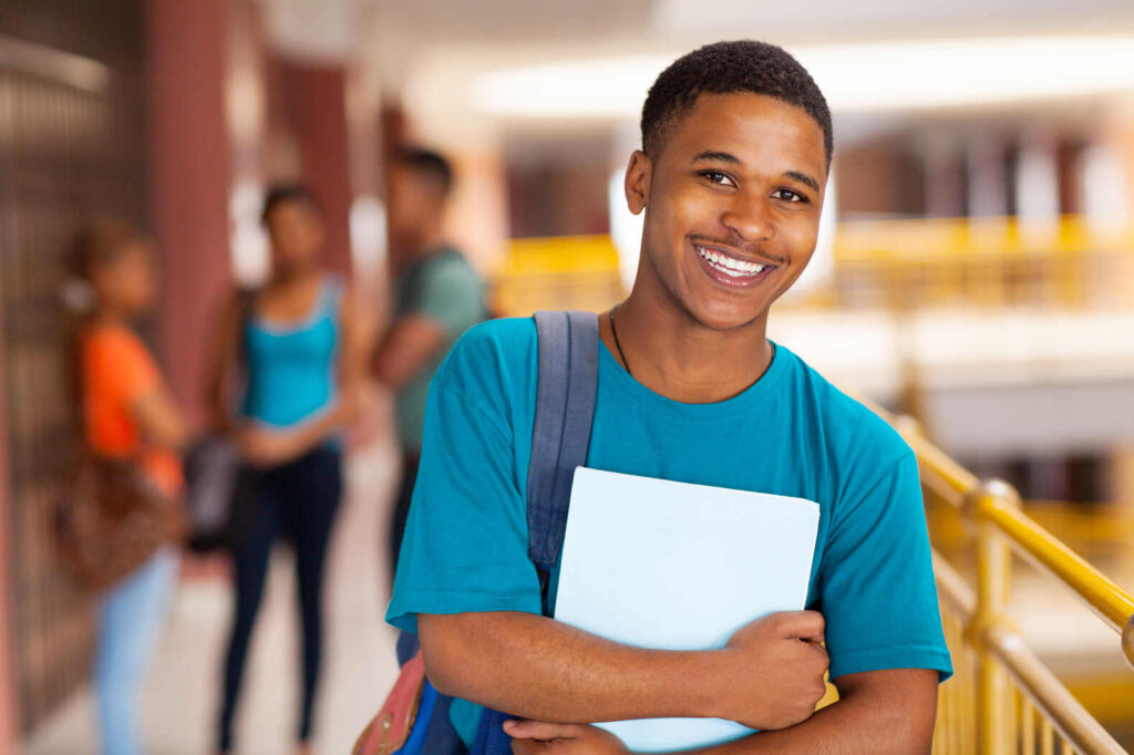 teen boy holding a book in the hallway of a school